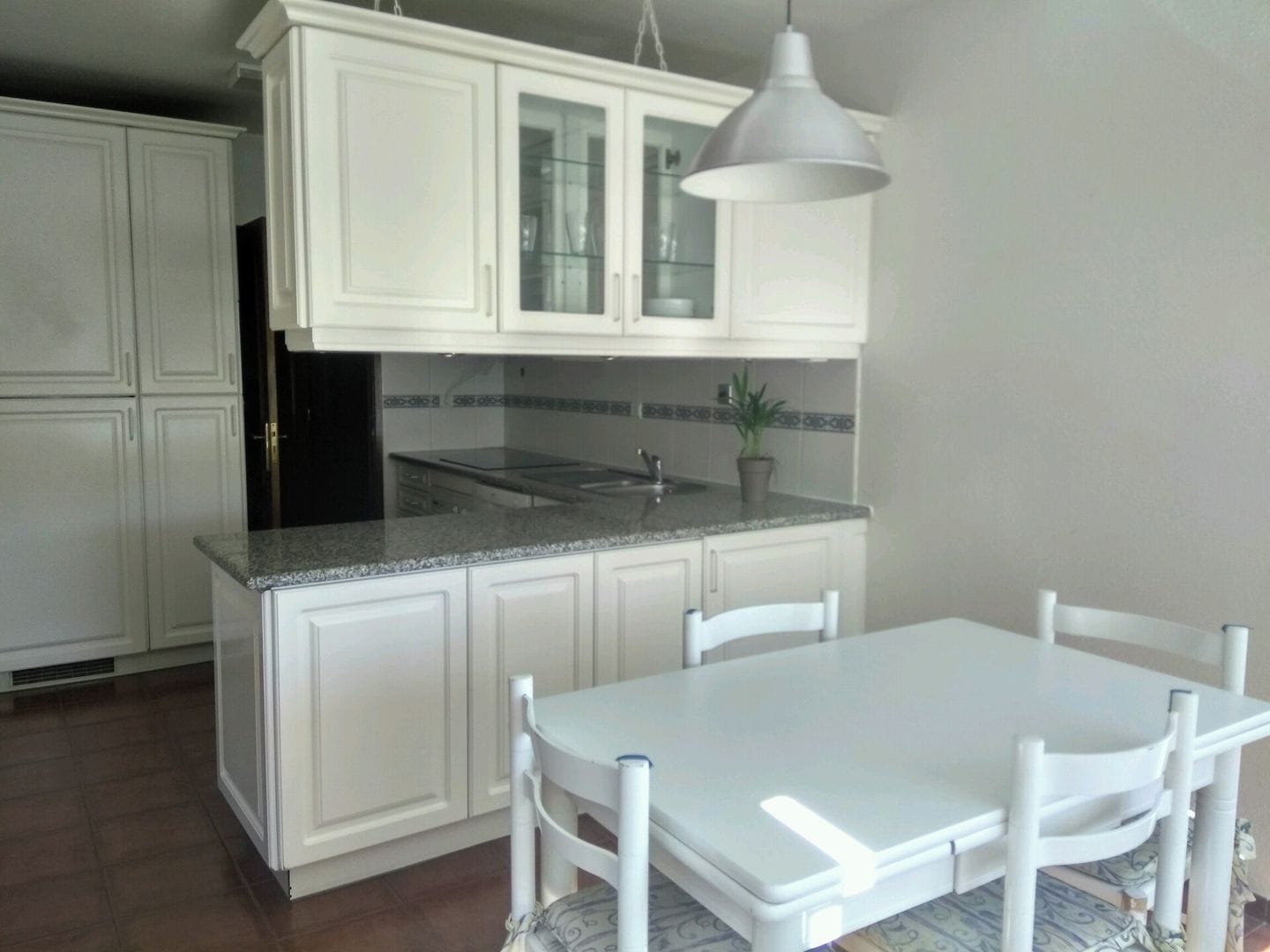 Una cocina con armarios blancos, encimera de granito, un lavabo y una mesa de comedor con sillas.