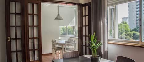 A dining area with a table, chairs, a potted plant, and a view of the outdoors through a window.