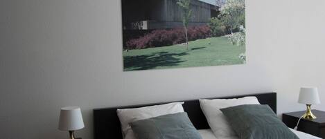 A bedroom with a bed, two bedside tables, and a wall-mounted picture.