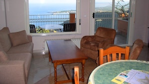 Sala de estar com sofá, mesa de madeira e vista para o mar através de uma grande janela.