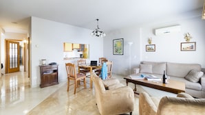 Uma sala de estar ampla, com um sofá, poltronas e um espaço de refeições com mesa e cadeiras.