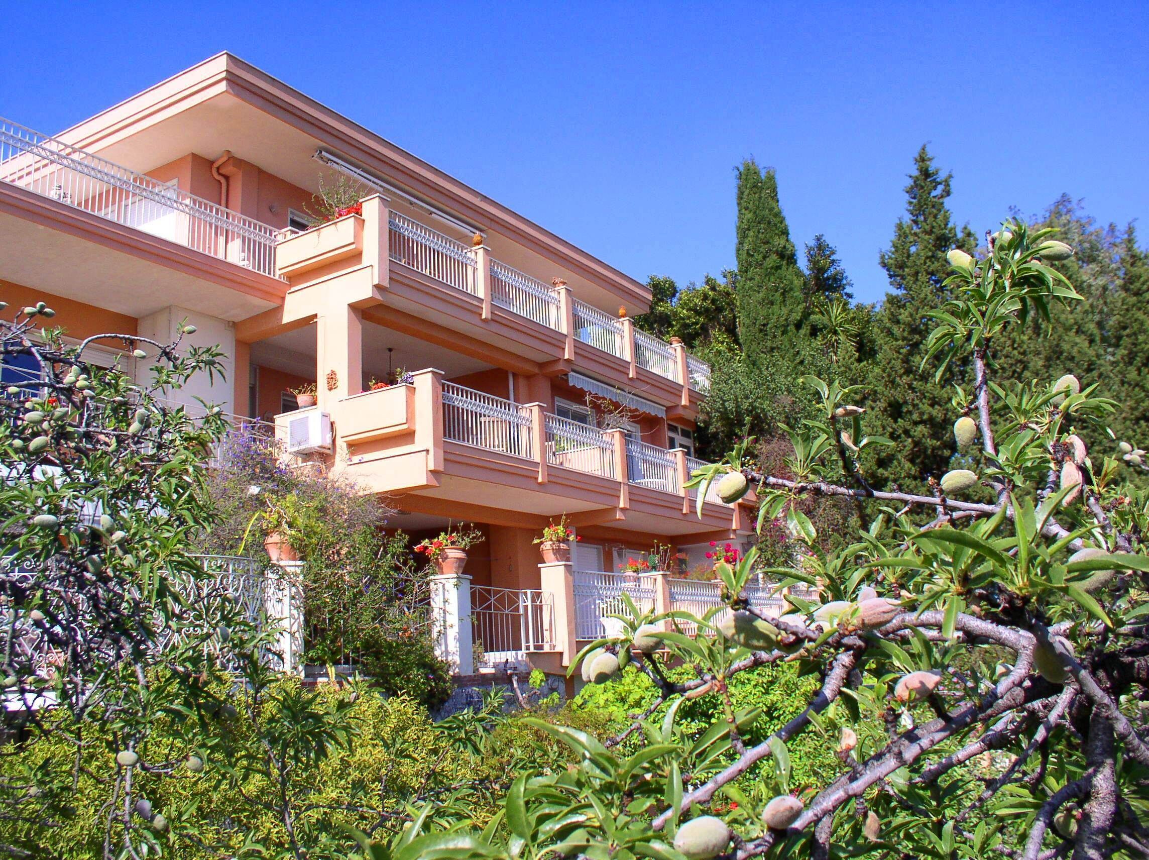 A multi-story building with balconies, surrounded by lush greenery and trees.
