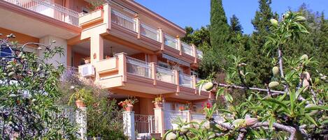 A multi-story building with balconies, surrounded by lush greenery and trees.