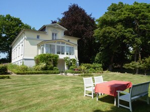 A large, light-colored building with a symmetrical facade, surrounded by well-maintained lawns and trees.