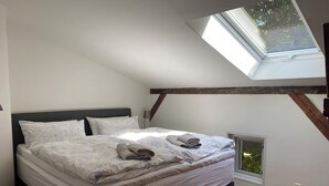 A bedroom with a skylight, a bed with floral bedding, and a small window.