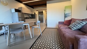 A modern kitchen with white cabinets, a dining area with a table and chairs, and a living area with a sofa and patterned rug. - Rivadige Suite 3 - Verona Journeys (Verona)