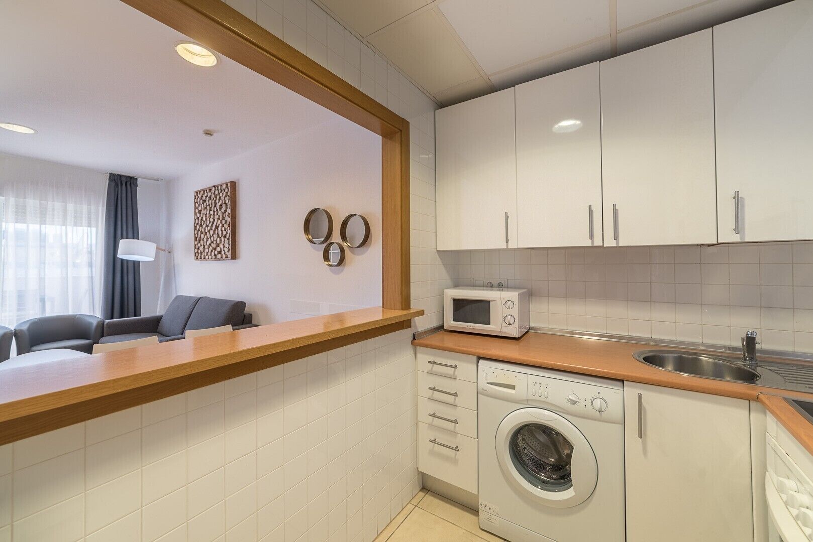 A compact kitchen with a microwave, washing machine, and a wooden countertop.