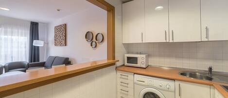A compact kitchen with a microwave, washing machine, and a wooden countertop.