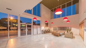 A spacious lobby with a modern design, featuring a reception desk, seating area, and large windows.