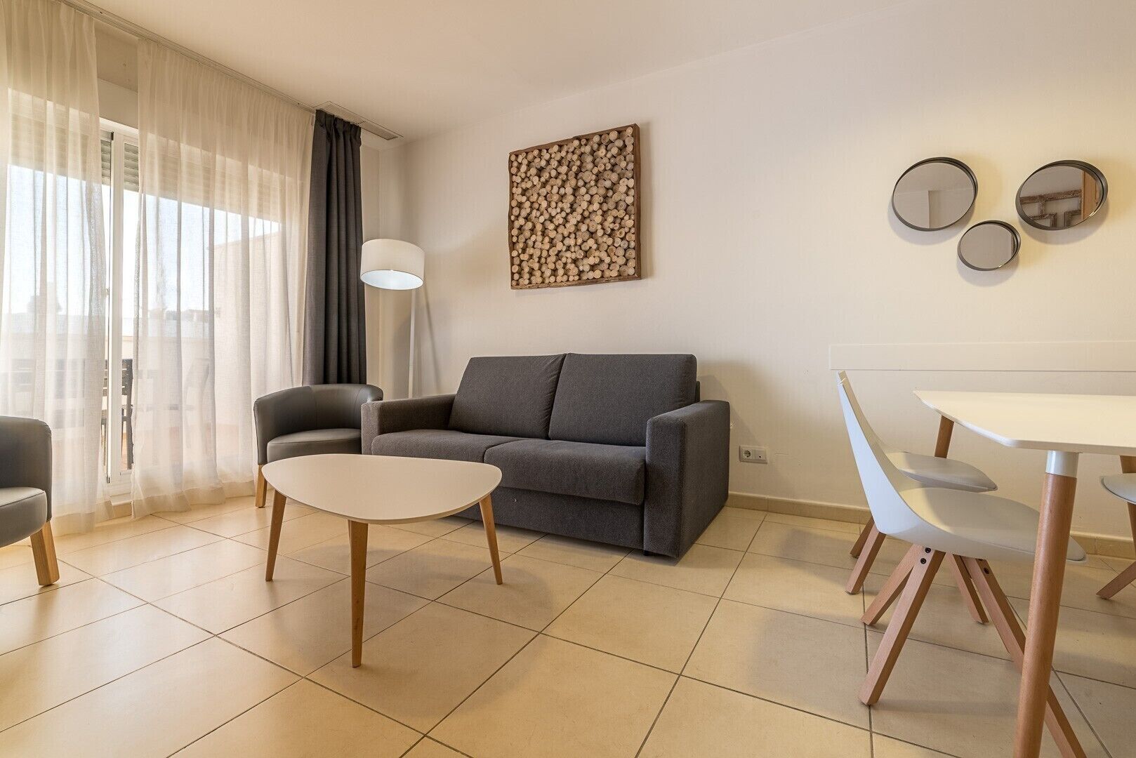 A modern living room with a grey sofa, a round coffee table, and a dining area with a white table and chairs.
