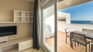 A balcony with a TV, a table, and chairs, overlooking a coastal view.