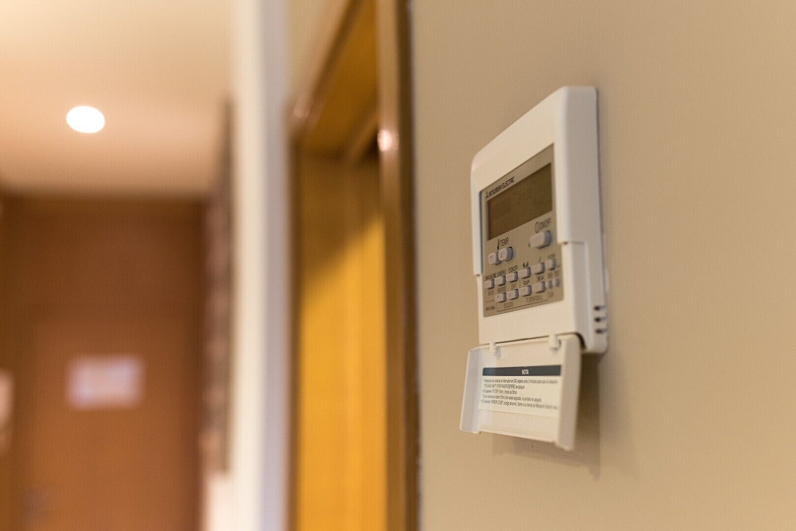 A wall-mounted thermostat with a digital display and control buttons.