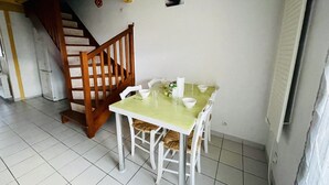Uma área de refeições com mesa, cadeiras, escada de madeira e uma geladeira.
