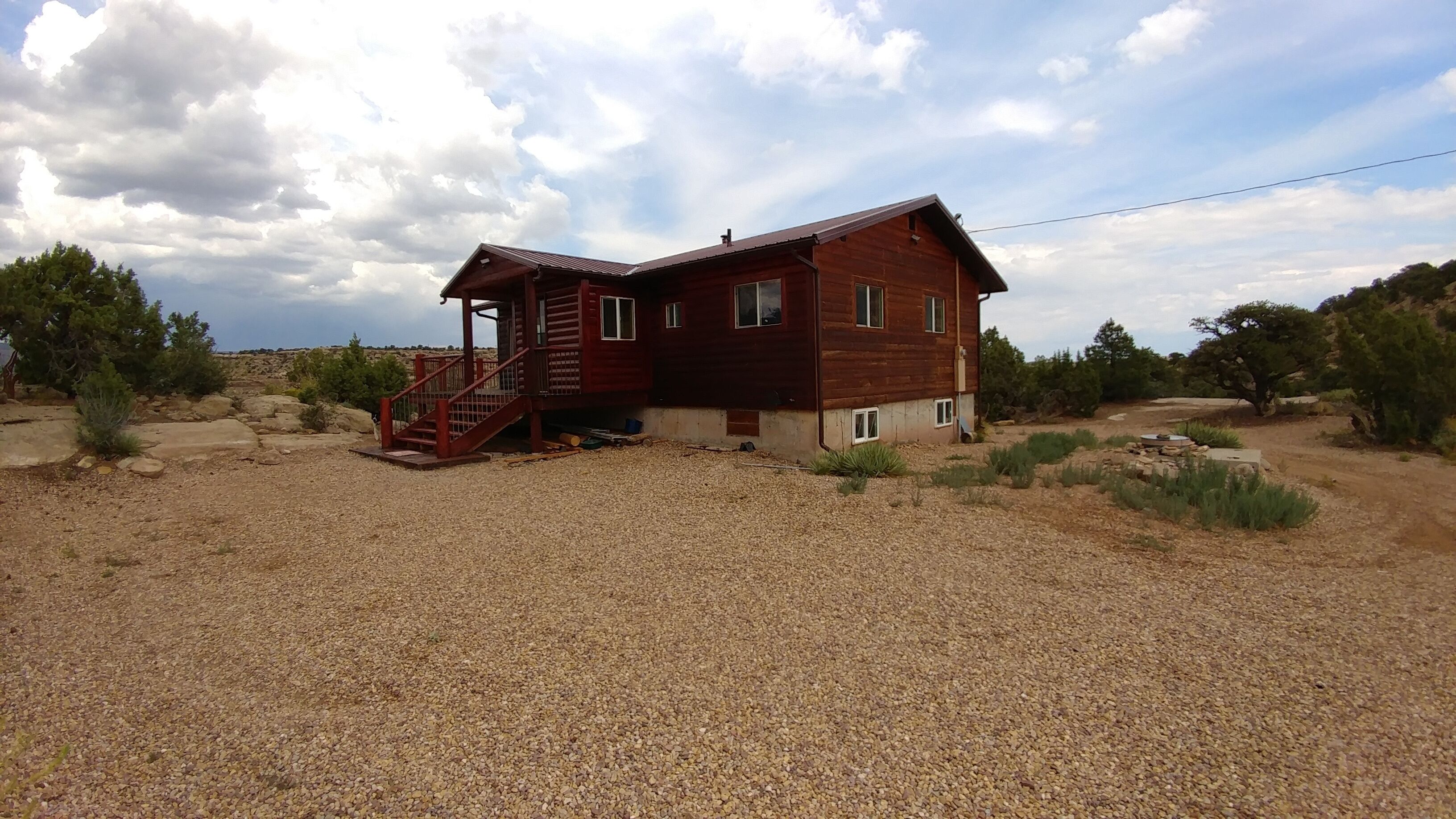 A wooden cabin with a porch and stairs, surrounded by gravel and sparse vegetation.