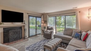 Un salón con chimenea, un televisor de pantalla plana grande, un sofá y vistas al exterior.