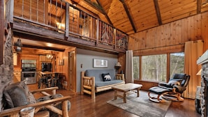 A spacious living area with a wooden floor, a sofa, a rocking chair, a dining table, and a kitchen in the background. - Circle J Lodge, Relaxing pet friendly cabin at Terry Peak with new hot tub! (Lead)