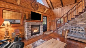 A log cabin interior with a stone fireplace, a mounted deer head, a television, and a staircase. - Circle J Lodge, Relaxing pet friendly cabin at Terry Peak with new hot tub! (Lead)