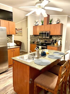 A kitchen with wooden cabinets, a stainless steel refrigerator, a microwave, and an oven. There is a ceiling fan above the kitchen island. - Fun in the Sun Lake Getaway (Lake Havasu City)