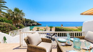 A terrace with wicker furniture, a dining table set with plates and glasses, and a view of the sea.