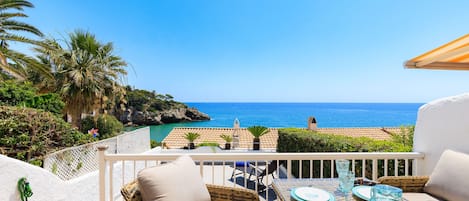 Eine Terrasse mit Korbmöbeln, einem Esstisch gedeckt mit Tellern und Gläsern und Blick aufs Meer.
