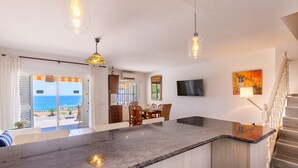 A modern kitchen with a large island, dining area, and a view of the sea.