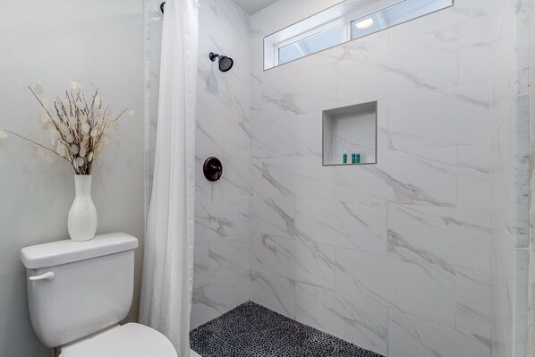 A bathroom with a toilet, shower, and a small shelf with toiletries. - Downtown Gilbert Getaway - Sleeps 8 (Gilbert)