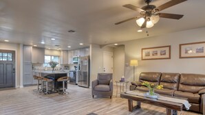 A spacious living area with a brown leather sofa, a coffee table with a vase, and a kitchen in the background. - Downtown Gilbert Getaway - Sleeps 8 (Gilbert)