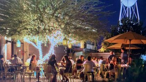 An outdoor dining area with tables and chairs, a water tower in the background, and a tree with lights. - Downtown Gilbert Getaway - Sleeps 8 (Gilbert)