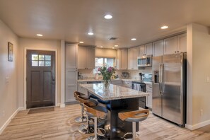 A modern kitchen with a central island, stainless steel appliances, and wooden bar stools.