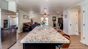 A modern kitchen with a large island, stainless steel appliances, and a dining area with wooden chairs. - Downtown Gilbert Getaway - Sleeps 8 (Gilbert)