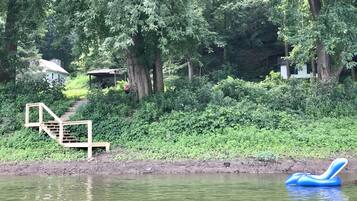 A serene lakeside setting with a wooden staircase leading to a covered area, surrounded by lush greenery and trees.