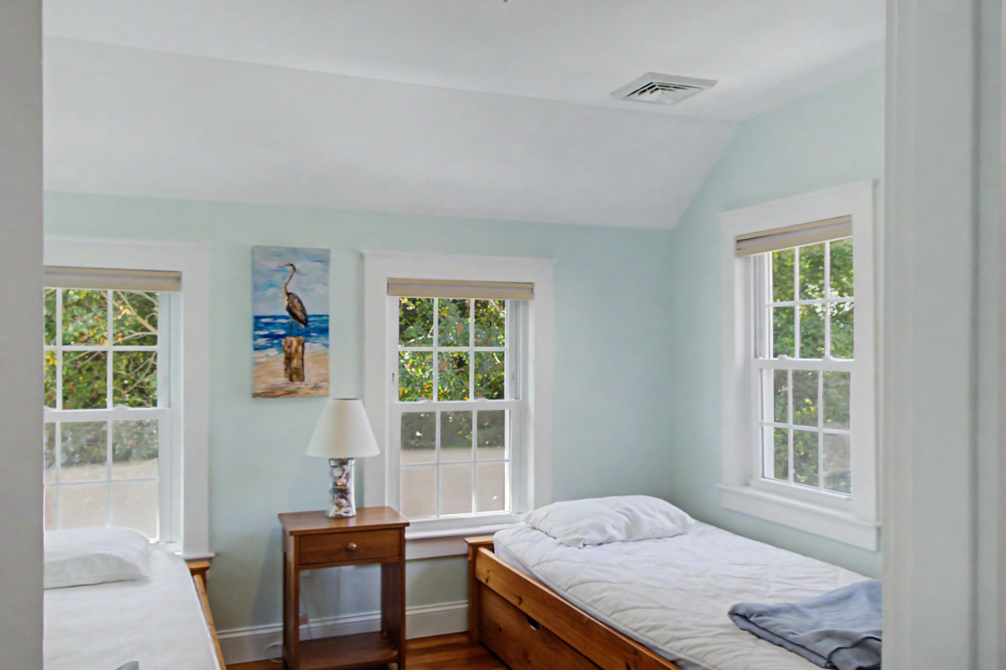 Une chambre avec deux lits, une table de chevet, une lampe et un tableau représentant un oiseau.