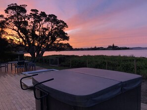 Uma banheira de hidromassagem em um deck com vista para o pôr do sol sobre a água.
