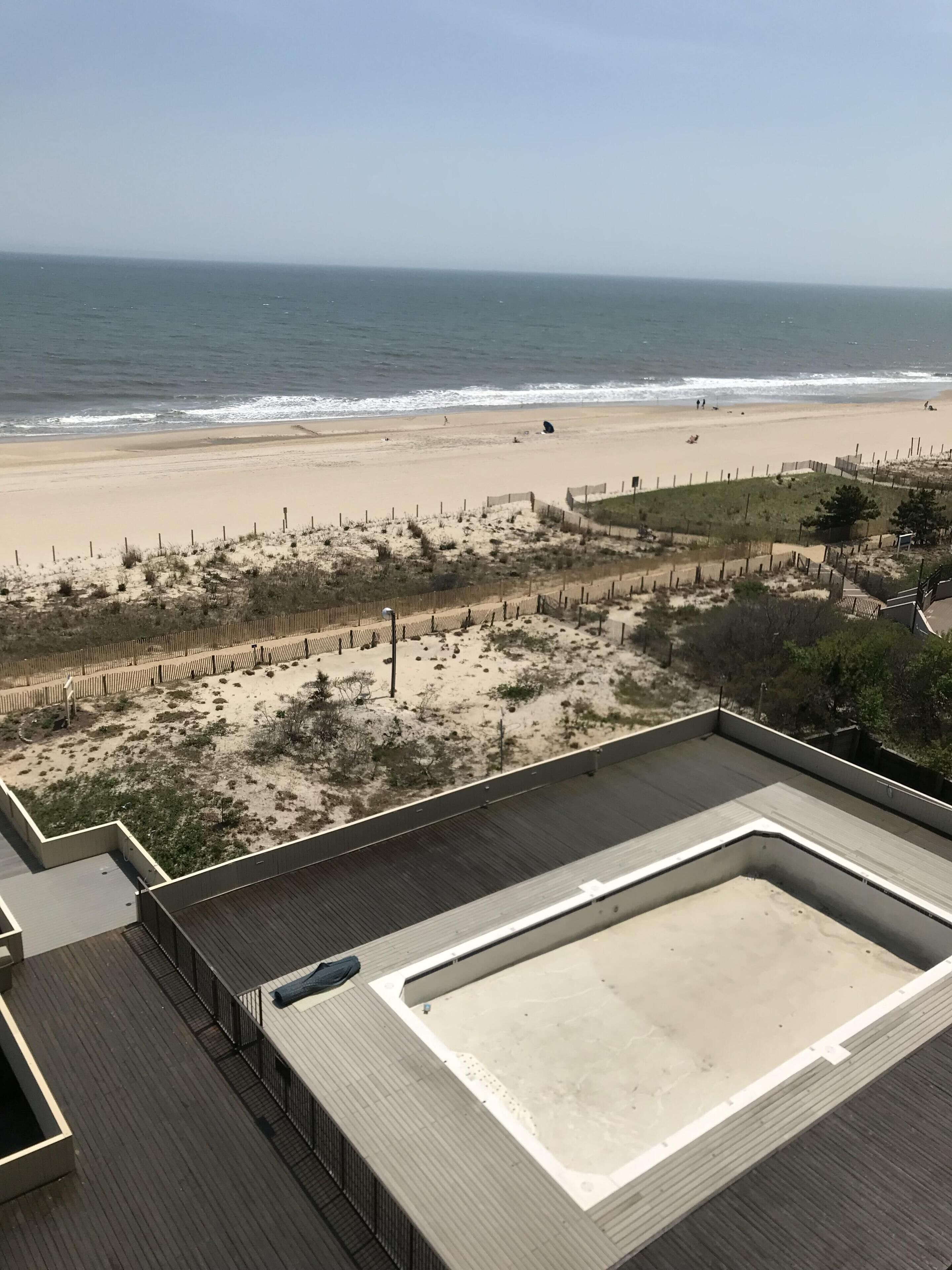 Vista a la playa desde una terraza en la azotea, con una zona de arena, valla de madera y una vista despejada del océano.