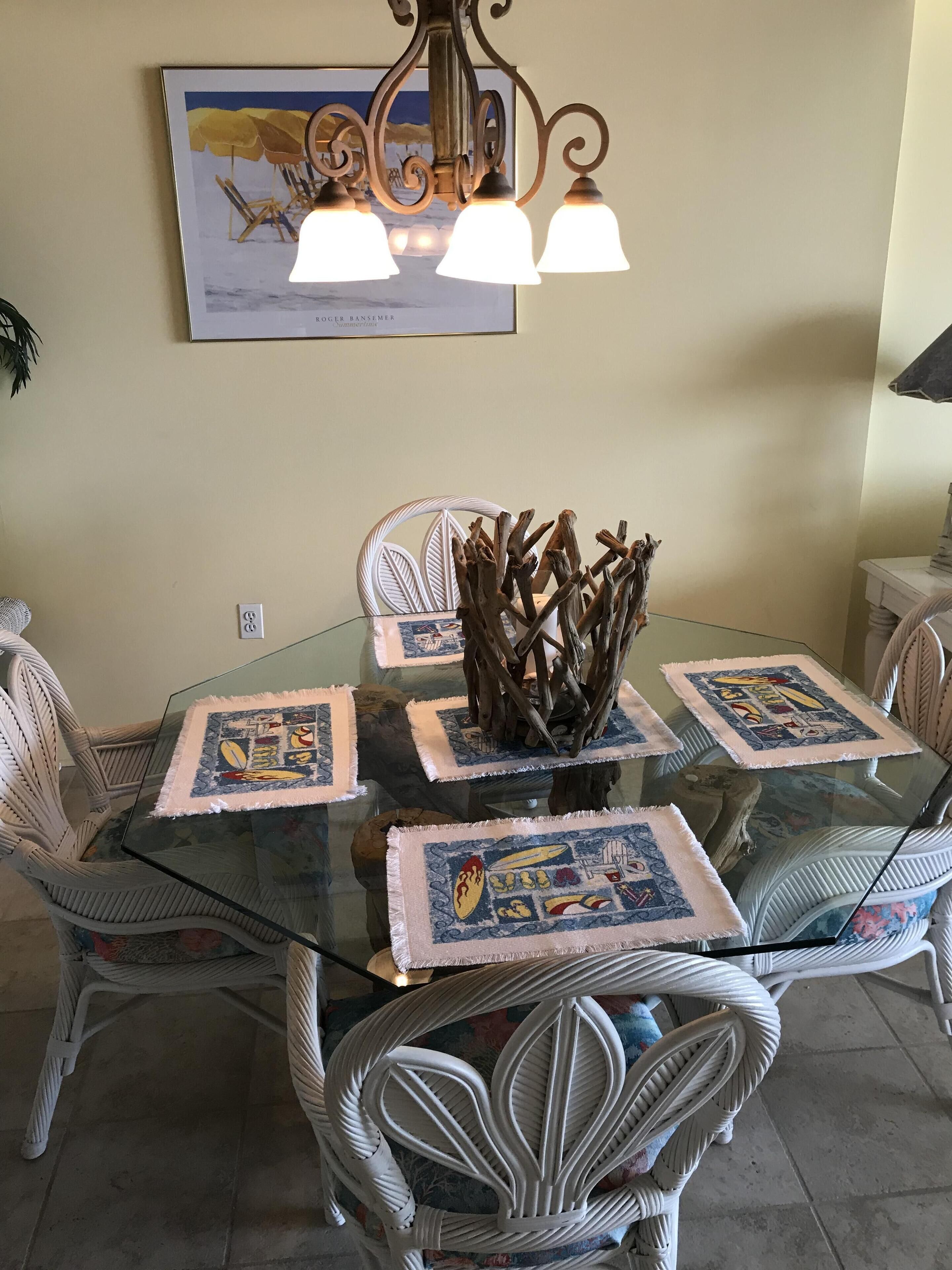 A dining table with glass top and white chairs, a chandelier, and a framed artwork on the wall.