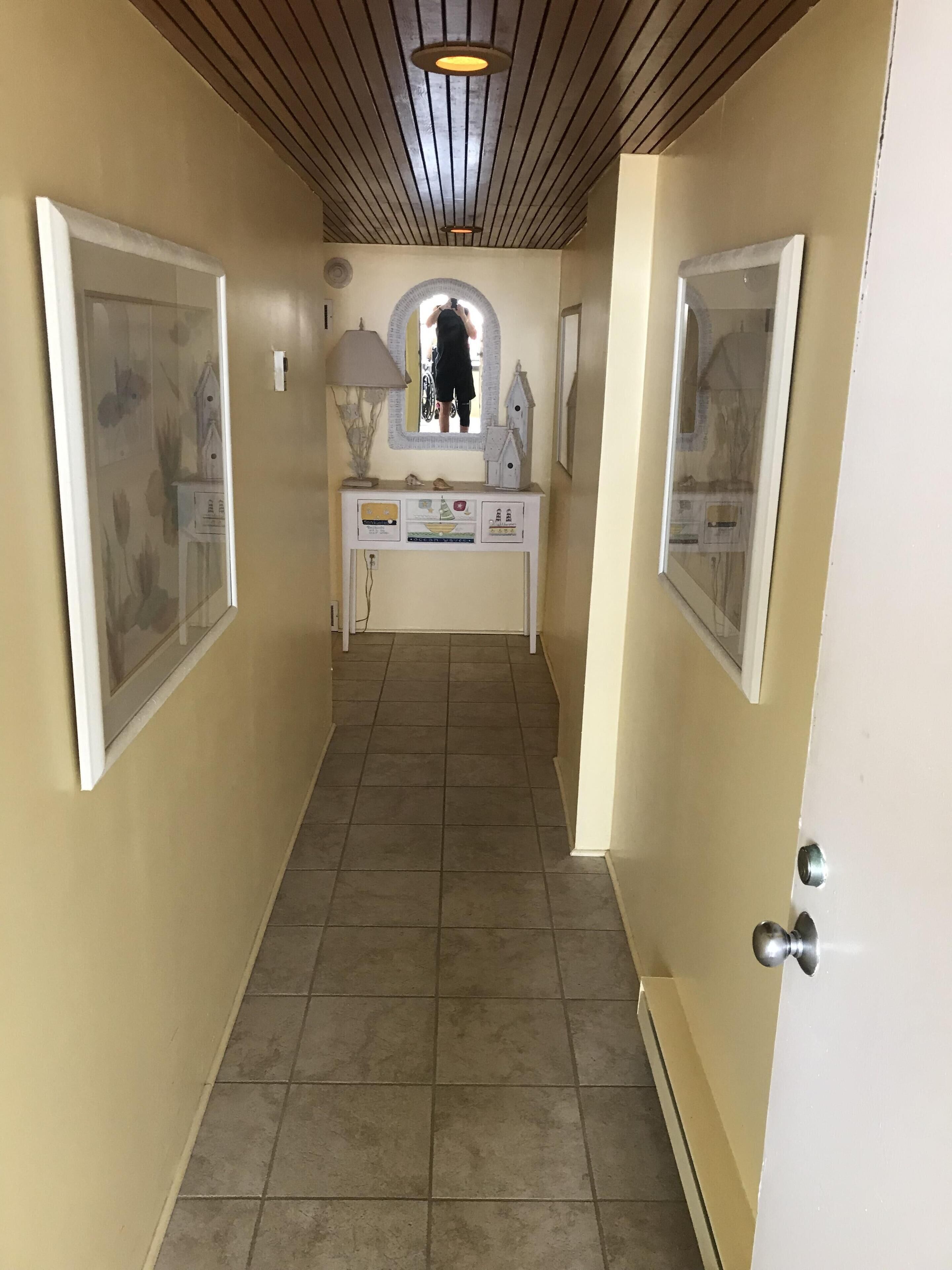 A hallway with a tiled floor, a white console table with decorative items, and framed pictures on the walls.
