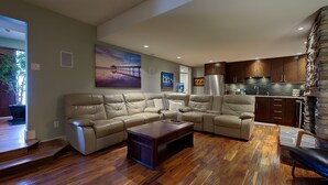 A spacious living room with a large L-shaped sectional sofa, a wooden coffee table, and a kitchen area with dark wooden cabinets and a stone accent wall. - 5-star Okanagan Getaway Pet Friendly, Privacy (Lake Country)