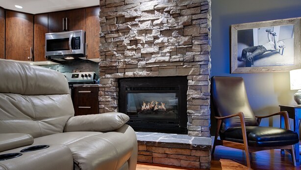 A living room with a stone fireplace, leather sofa, and a mounted TV. - 5-star Okanagan Getaway Pet Friendly, Privacy (Lake Country)