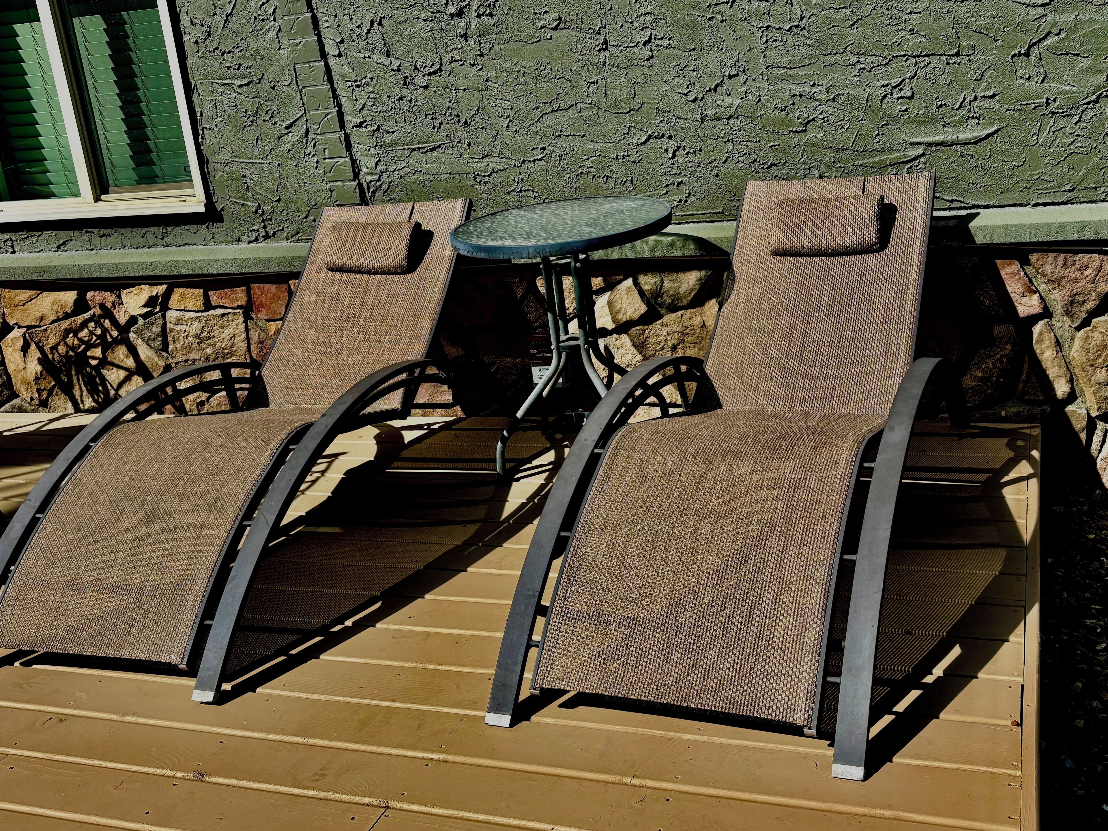 Outdoor seating with chairs and a table, a stone wall, and a window with blinds.