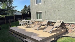 A deck with outdoor furniture, including chairs and a table, surrounded by a stone wall and a grassy area. - 5-star Okanagan Getaway Pet Friendly, Privacy (Lake Country)
