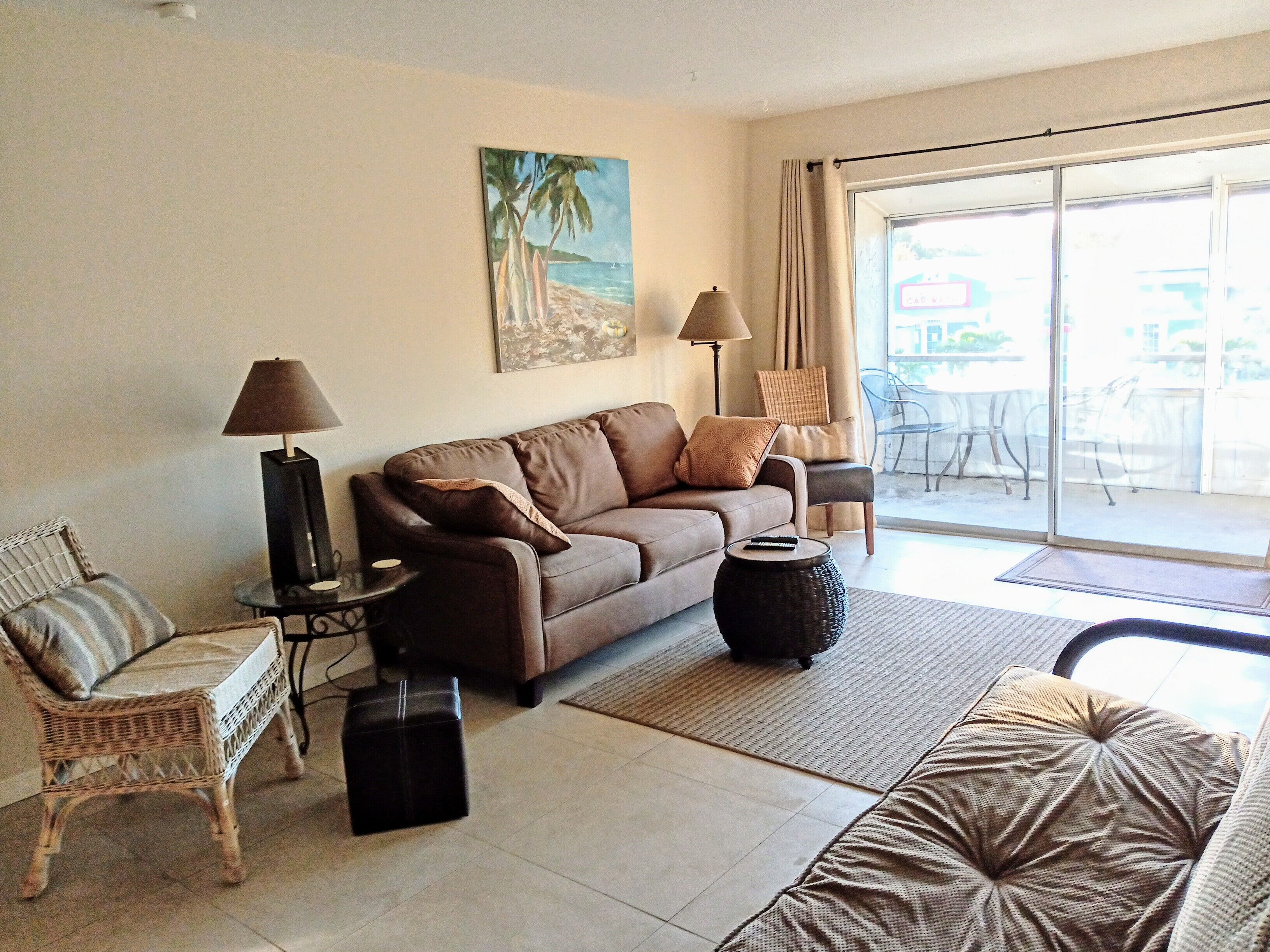 A living room with a brown sofa, two armchairs, a coffee table, and a painting of a beach scene.