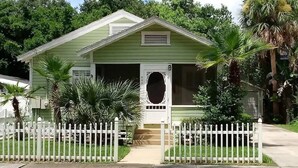 Een gelijkvloers huis met een groene gevel, een witte hek en een veranda.