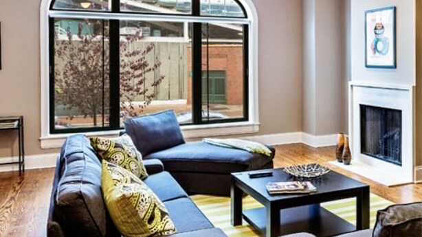 A living room with a large arched window, a fireplace, and a sofa with patterned cushions.