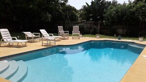 A rectangular swimming pool with a tiled edge, surrounded by a concrete deck. There are several white lounge chairs arranged around the pool. - 3 bedroom, 2 bath,  pool home that sleeps 6, with screened back patio (Palm Harbor)