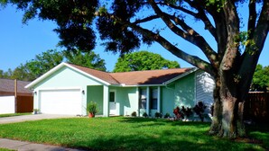 A single-story house with a garage, a front porch, and a lawn. - 3 bedroom, 2 bath,  pool home that sleeps 6, with screened back patio (Palm Harbor)