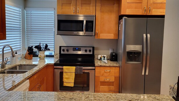 A kitchen with granite countertops, stainless steel appliances, wooden cabinets, and a window with blinds. - 3 bedroom, 2 bath,  pool home that sleeps 6, with screened back patio (Palm Harbor)
