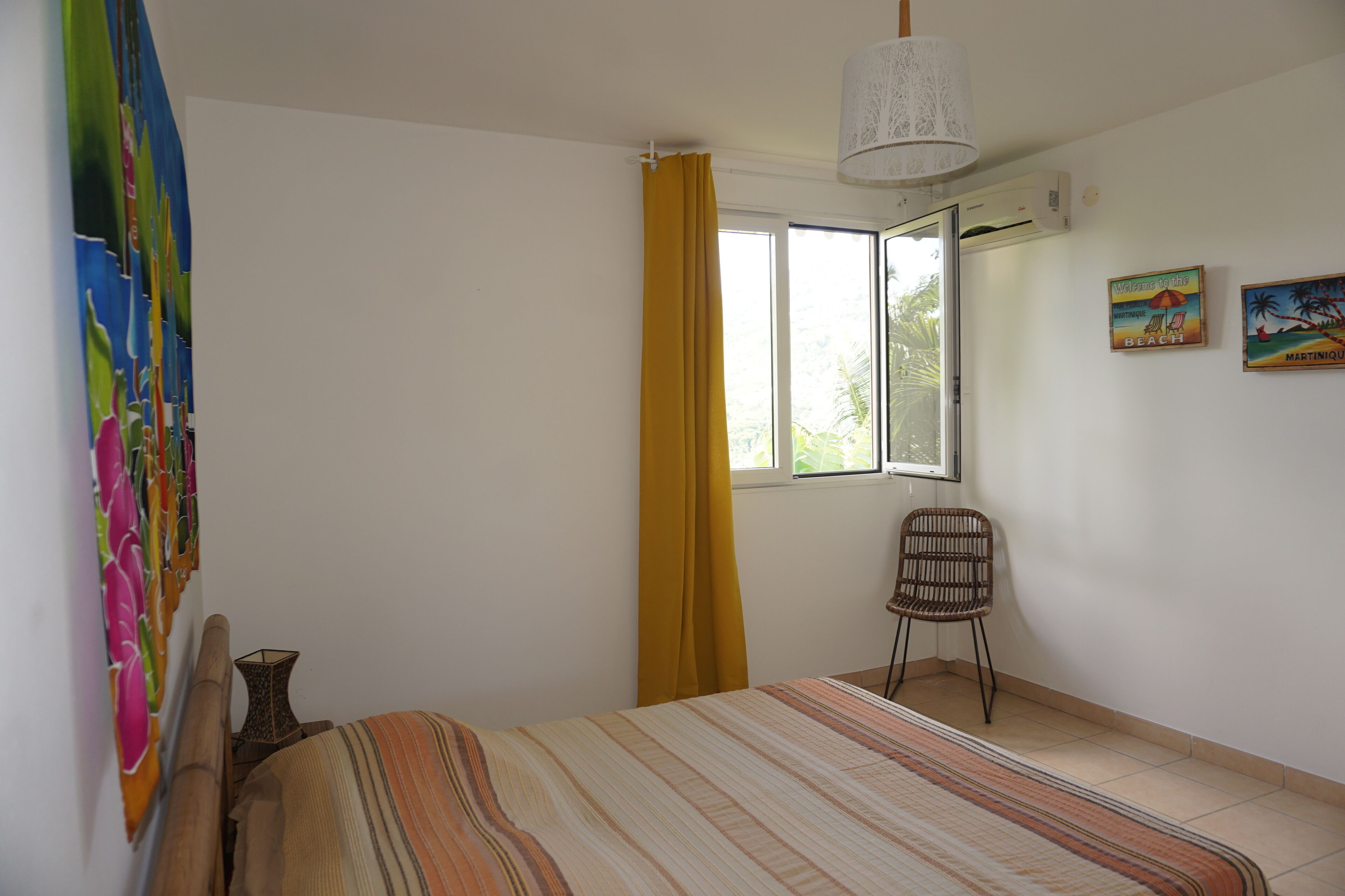 Une chambre à coucher avec un lit, une chaise, une fenêtre avec des rideaux jaunes et un mur orné d’un tableau.