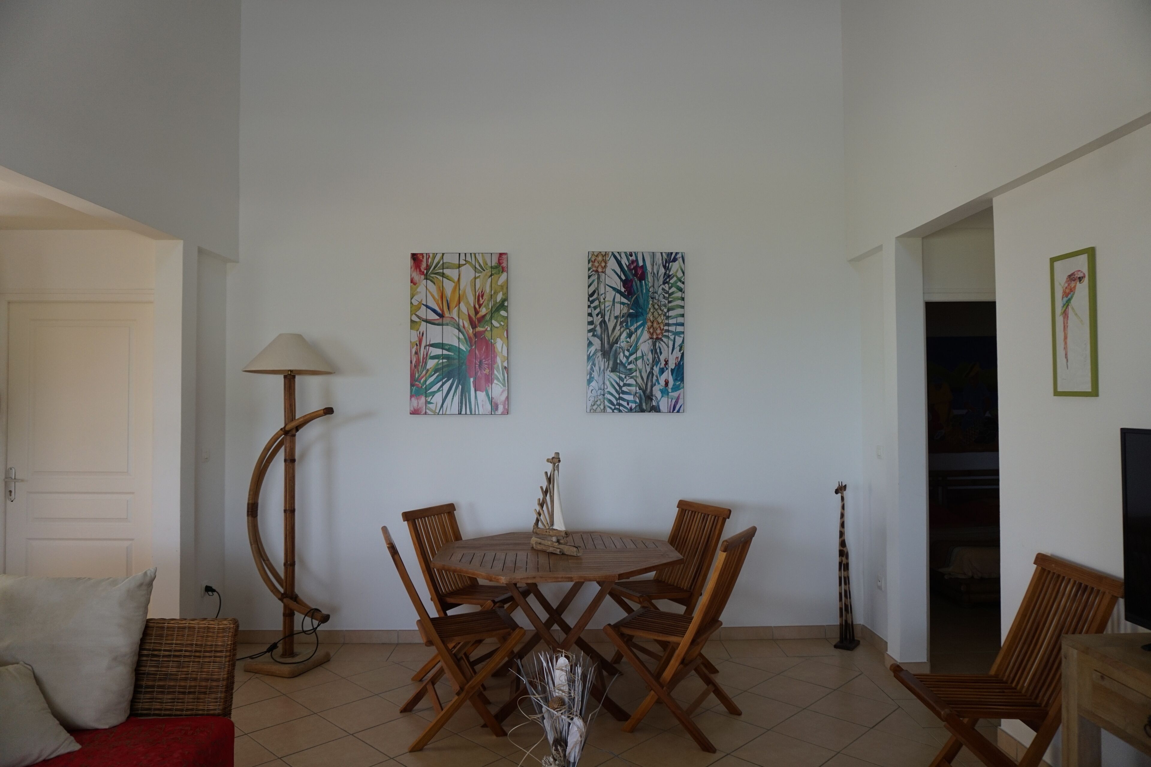 A dining area with a round wooden table and four chairs, a lamp, and two wall-mounted paintings.
