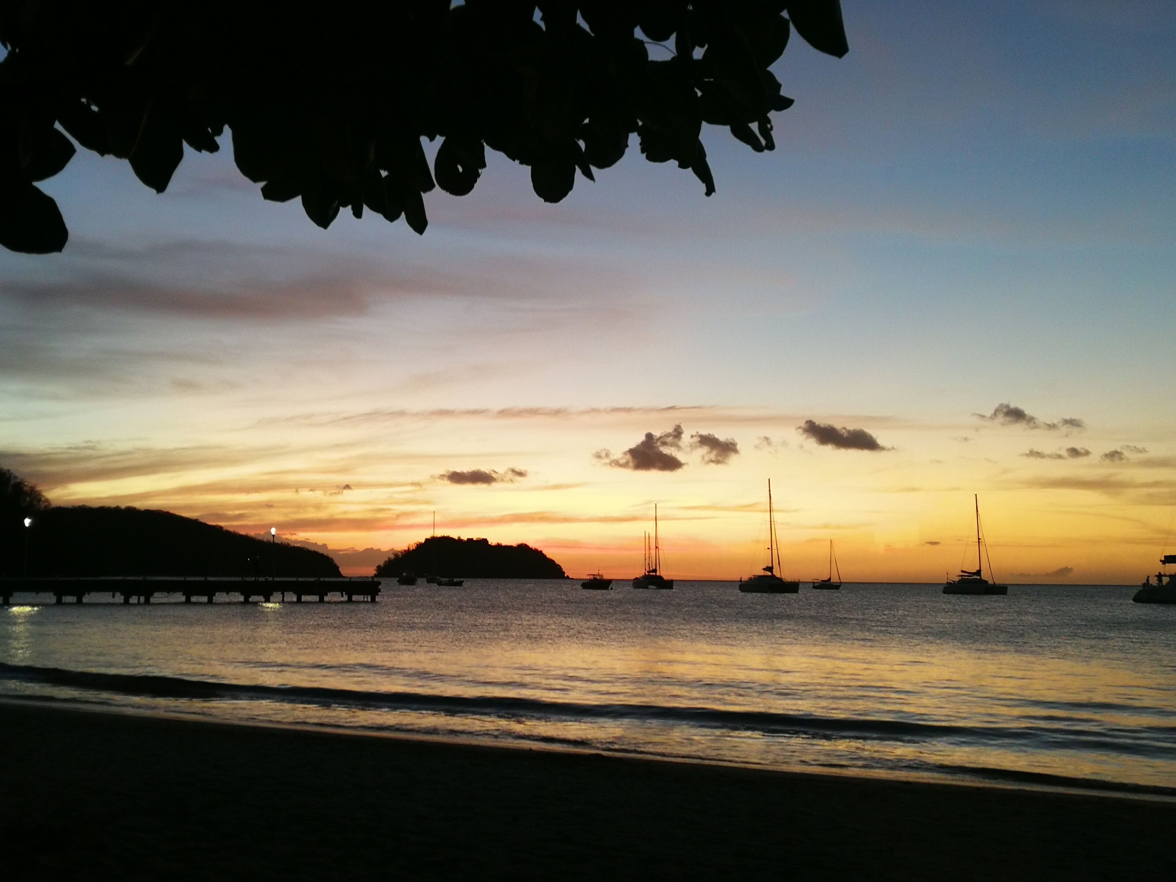 Un atardecer sobre un mar tranquilo con varios veleros anclados.