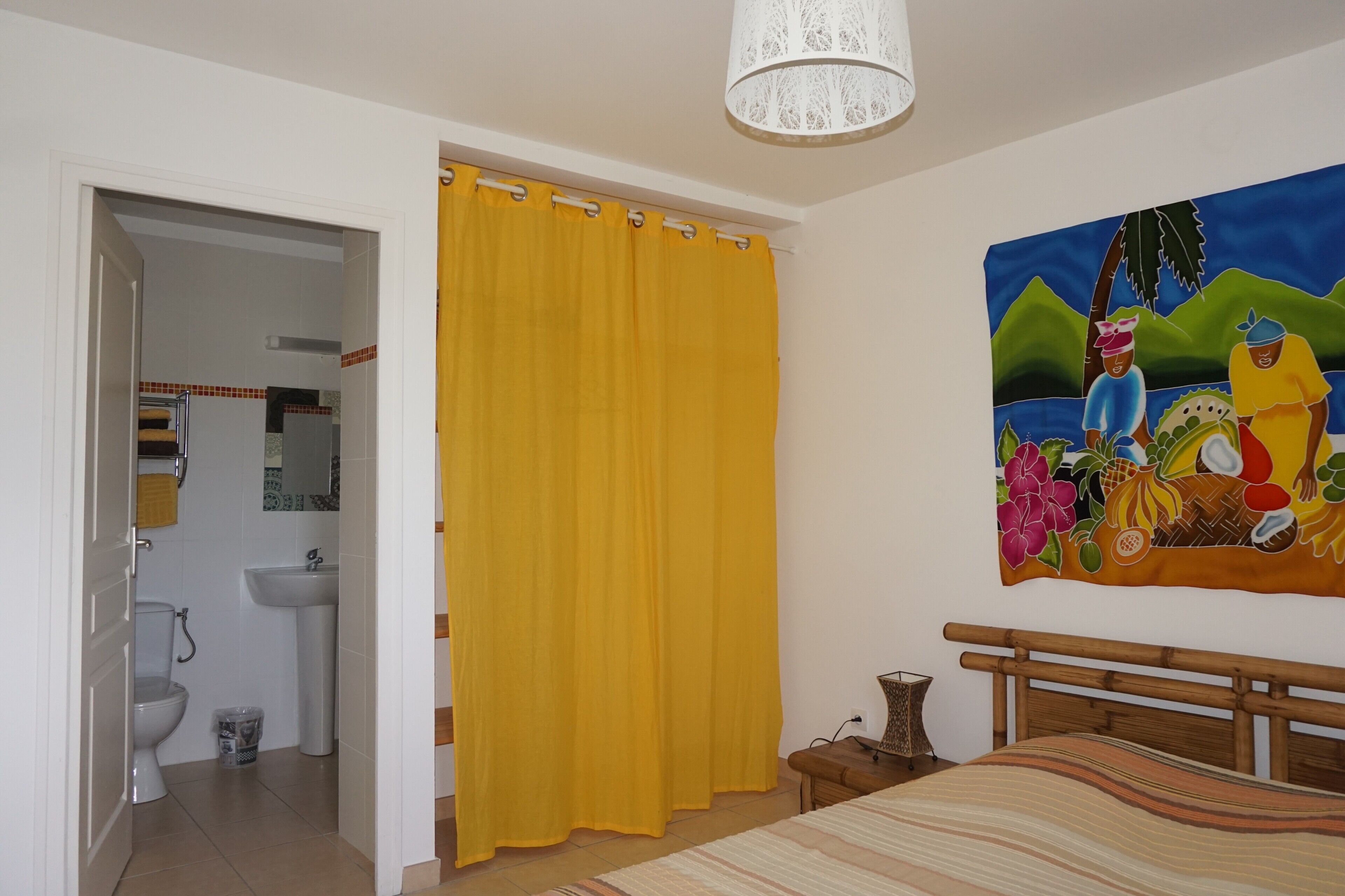 A bedroom with a bed, a painting, and a bathroom visible through an open door.
